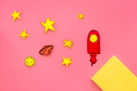 Literature about cosmos for school children. Book with blank cover near cutout of rocket, stars, moon on pink background top view mockupの写真素材