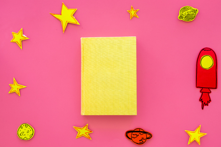 Literature about cosmos for school children. Book with blank cover near cutout of rocket, stars, moon on pink background top view mockup.の写真素材