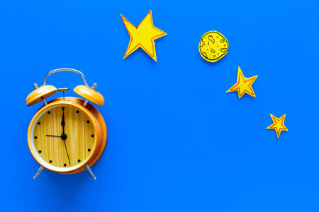 Sleep time, clock on the bed concept. Alarm clock near moon and stars cutout on blue background top...