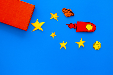 Literature for children. Fantactic, fiction story. Book with blank cover near cutout of rocket, stars, moon on blue background top view mockup space for textの写真素材