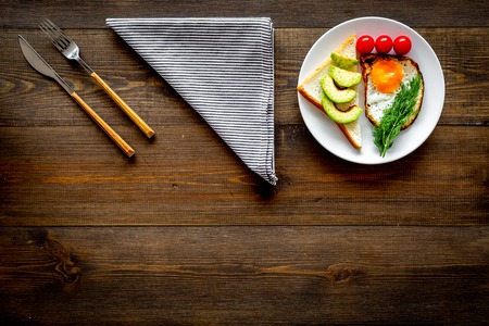 Healthy hearty breakfast. Fried eggs with vegetables near toast with avocado on dark wooden background copy spaceの写真素材
