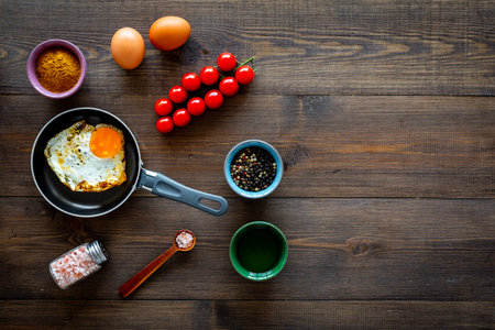 Ingredients for fried eggs with vegetables. Ready eggs in a frying pan near cherry tomatoes, greenery, spices, raw eggs on dark wooden background top view space for textの写真素材