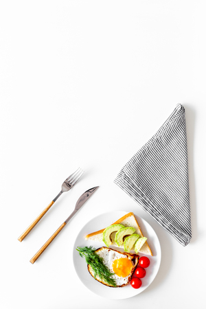 Lunch rich fiber and protein. Fried eggs with vegetables near toast with avocado on white background top view.の写真素材