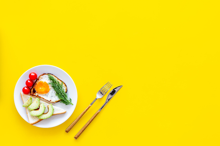 Healthy hearty breakfast. Fried eggs with vegetables near toast with avocado on yellow background top view.の写真素材