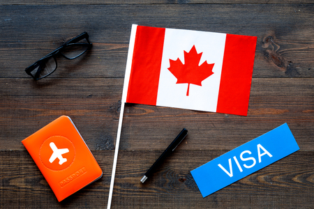Visa to Canada concept. Text visa near passport cover and canadian flag on dark wooden background top viewの写真素材