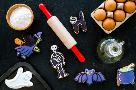 Cooking halloween gingerbread cookies concept. Glazed cookies, ingredients, crockery on black wooden...