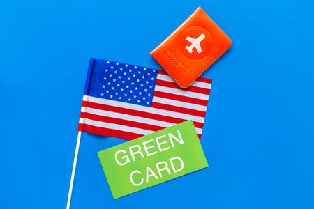 Green card text near passport cover and USA flag top view on blue background copy space. Immigration to United states of americaの写真素材