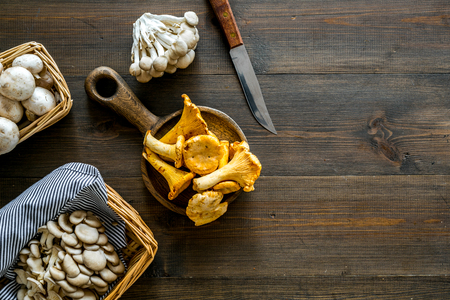 Collect mushroom concept. Champignons, oysters, chanterelles in basket near knife on dark wooden background top view.の写真素材