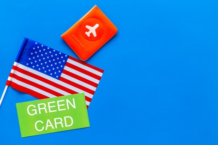 Green card text near passport cover and USA flag top view on blue background copy space. Immigration to United states of America.の写真素材