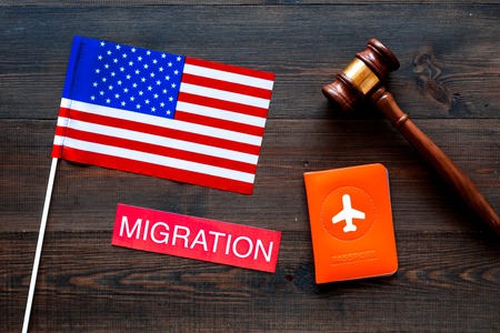 Immigration to United States of America concept. Text immigration near passport cover and USA flag on dark wooden background top view.の写真素材