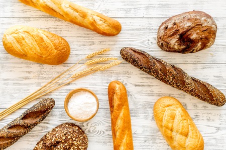 Set of fresh homemade bread. Bread assortment. Loaf, baguette. White and brown bread on tablecloth near ears and bowl with flour on white wooden background top viewの写真素材