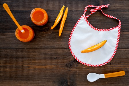 Baby food concept. Pumpkin puree in bowl near bib, pumpkin slices, spoon on dark wooden background top view.の写真素材