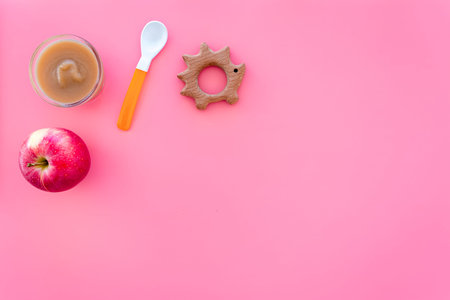 Baby food concept. Apple puree in bowl near apple, spoon on pink background top view.の写真素材