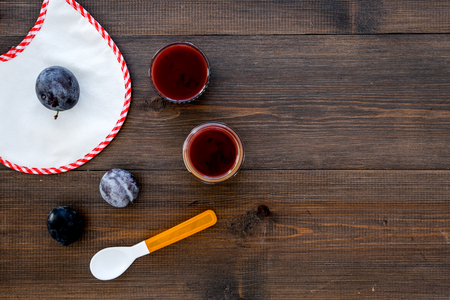 Fruit puree for small babies. Puree with prunes in bowl near punes, spoon, bib on dark wooden background top view copy spaceの写真素材