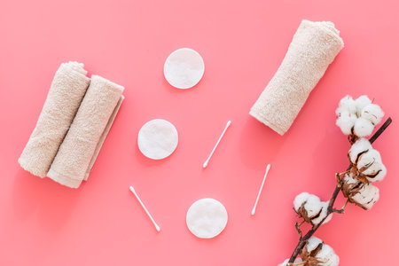 Products made of cotton. Bath accessories. Towels, cotton pads and swabs near dry cotton flowers on pink background top viewの写真素材