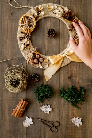 Make creative christmas wreath of thread. Female hand hold wreath near matherial for decorative element on dark wooden background top viewの写真素材