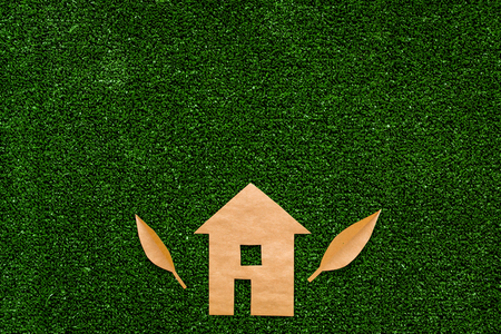 Green energy for home concept. Care for environment. House cutout made of craft paper on green grass background top view.の写真素材