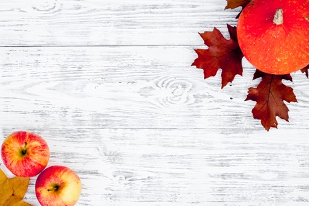 Composition with autumn vegetables and leaves in red and orange colors. Brown dried leaves, pumpkin, apple on white wooden background top view.の写真素材