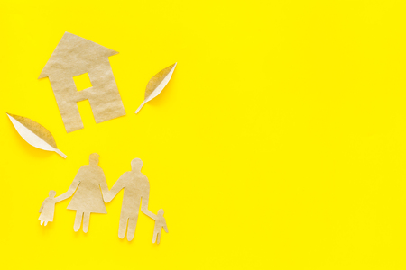 Green energy for home concept. Care for environment. House cutout made of craft paper near family cutout on yellow background top view.の写真素材