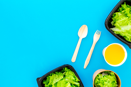 Food delivery concept. Healthy food. Diet meal with lettuce in plastic boxes, green tea, disposable tableware on blue background top view.の写真素材
