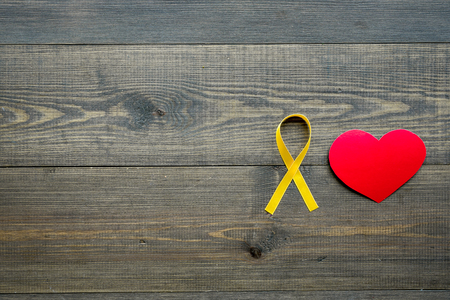 Endometriosis. Gynecological diseases concept. Symbolic yellow ribbon near heart sign on dark wooden background top view.の写真素材