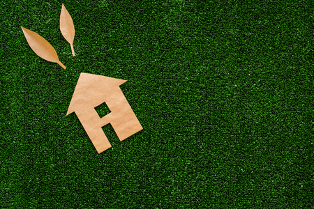 Green energy for home concept. Care for environment. House cutout made of craft paper on green grass background top view copy spaceの写真素材