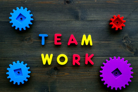 Teamwork concept. Text teamwork lined with colored letters near toy gears on dark wooden background...