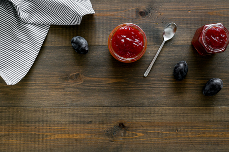Fruit dessert. Plum jam in jar near fresh plums and spoon on dark wooden background top view copy spaceの写真素材