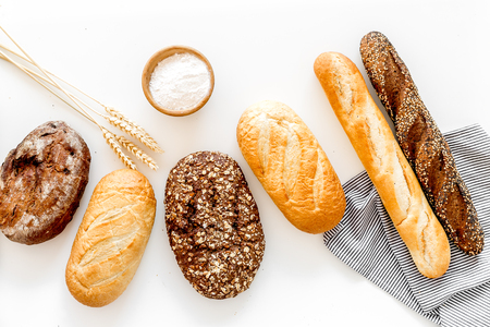 Set of fresh homemade bread. Bread assortment. Loaf, baguette. White and brown bread on tablecloth near ears and bowl with flour on white background top viewの写真素材