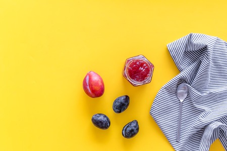 Fruit dessert. Plum jam in jar near fresh plums and spoon on yellow background top view copy spaceの写真素材