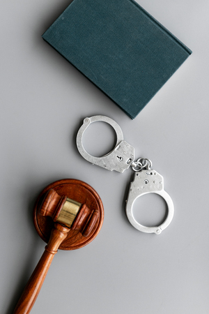 Arrest concept. Metal handcuffs near judge gavel and law book on grey background top viewの写真素材