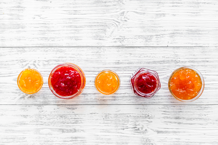 Set of sweet jams in glass jars on white wooden background top view.の写真素材