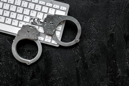 Cyber fraud concept. Handcuff near keyboard on black background top view space for text closeupの写真素材