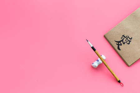 Chinese traditional calligraphy concept. Asian hieroglyph symbol in craft paper notebook near special writting pen on pink background top view.の写真素材