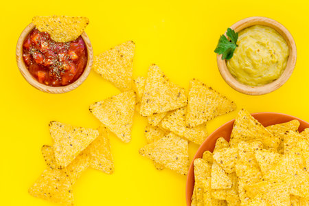 Snack for party. Mexican nachos near salsa and guacamole sause on yellow background top view.