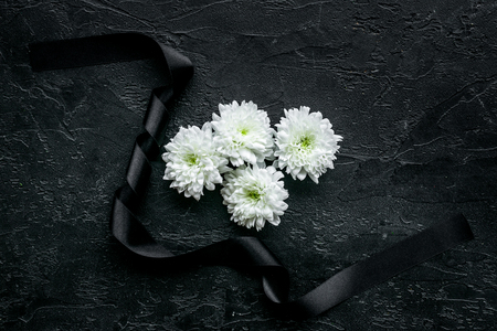 Funeral symbols. White flower near black ribbon on black background top view space for textの写真素材