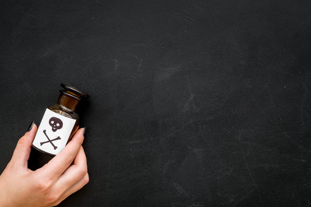 Dangerous addictions, dangerous entertainment. Poison. Female hand hold bottle with skull and crossbones on black background top view copy spaceの写真素材
