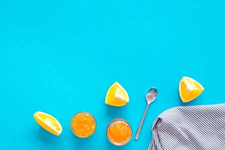 Fruit dessert. Orange jam in jar near slices of fresh oranges and spoon on blue background top view copy spaceの写真素材