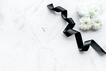 Funeral symbols. White flower near black ribbon on white stone background top view copy spaceの写真素材
