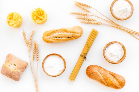 Products made of wheat flour. White flour in bowl, wheat ears, fresh bread and raw pasta on white background top viewの写真素材