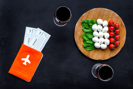 Gastronomical tourism. Italian food symbols. Passport and tickets near italian food like cheese, tomato, wine on black background top view copy spaceの写真素材