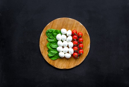 Italian flag made of mozzarella cheese, cherry tomatoes, green basil on wooden cutting board on black background top view space for textの写真素材