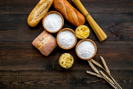 Bakery production, making bread and pasta. Fresh bread and raw pasta near flour in bowl and wheat ears on dark wooden background top view copy spaceの写真素材