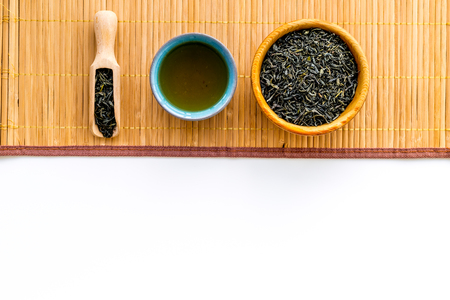 Chinese tea concept. Tea ceremony. Dry tea leaves in bowl and wooden scoop near cup of tea on white background and bamboo table mat top view copy spaceの写真素材