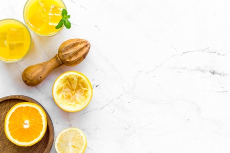 Make orange juice. Juice in glass near half cut oranges and jucier on white stone background top view copy spaceの写真素材