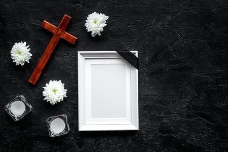 Funeral. Mockup of portrait of the deceased, of dead person. Frame with black ribbon near flowers, candles and cross on black background top view copy spaceの写真素材
