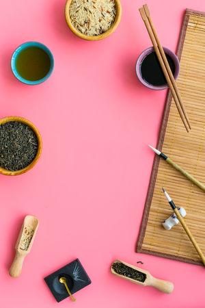 Chinese traditional symbols concept. Tea, rice, hieroglyph love, bambootabe mat, chopsticks, soy sause on pink background top view frame.の写真素材