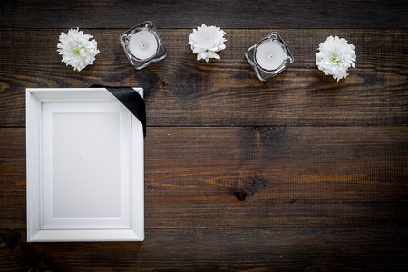 Death concept. Photo frame, mockup with black ribbon near flowers, candles on dark wooden background top view.の写真素材