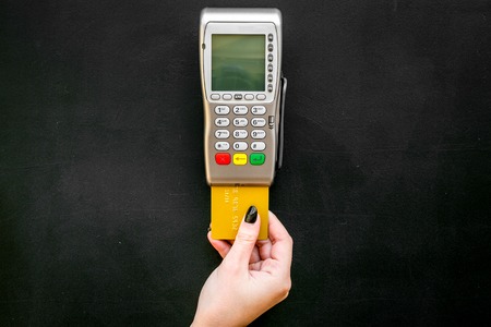 Pay by payment terminal. Woman's hand inserts credit card to terminal on black background top view.の写真素材