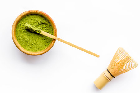 Matcha powder in bowl near specail stick and whisk on white background top view.